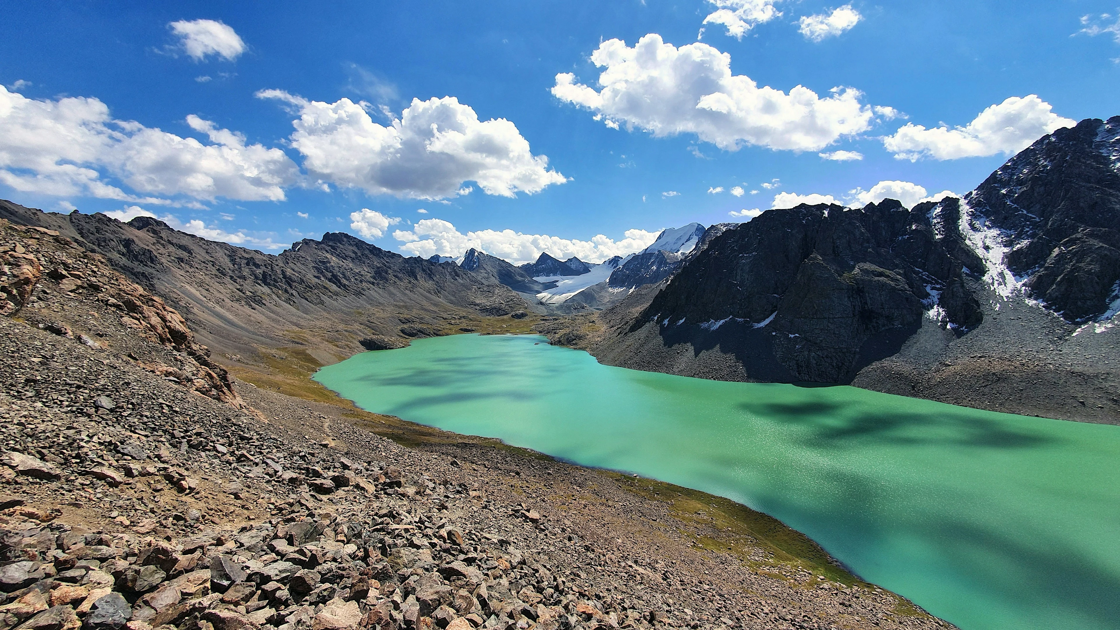 Turquoise Ala-Kul beneath sunlit rocky peaks and a blue summer sky