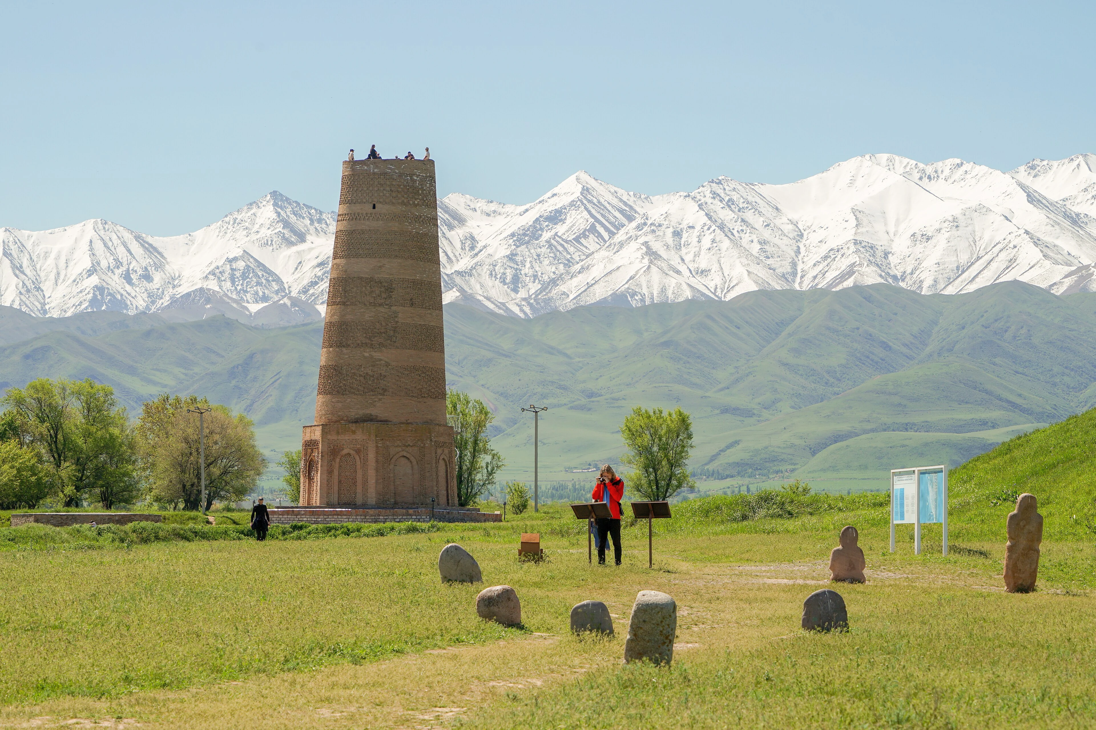 Burana Tower and balbal stone figures beneath a mountain backdrop.