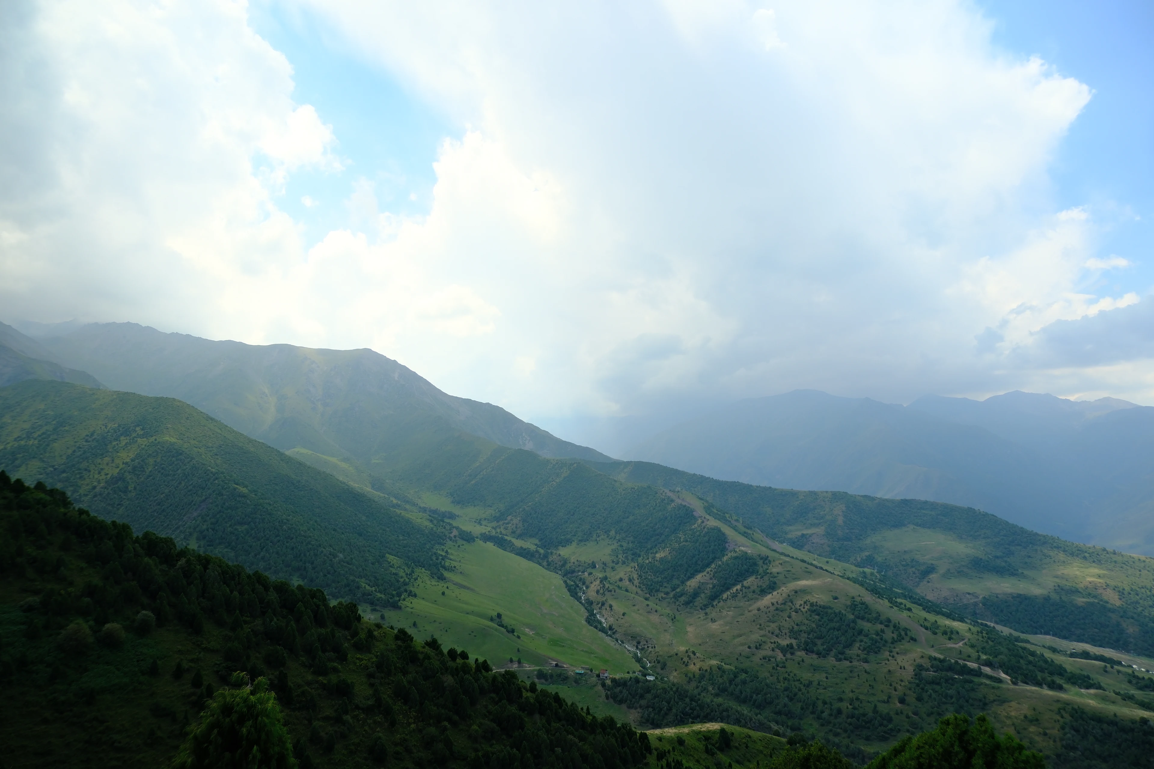 Clouds and sunlight above the green ridgelines of the Alamedin area.