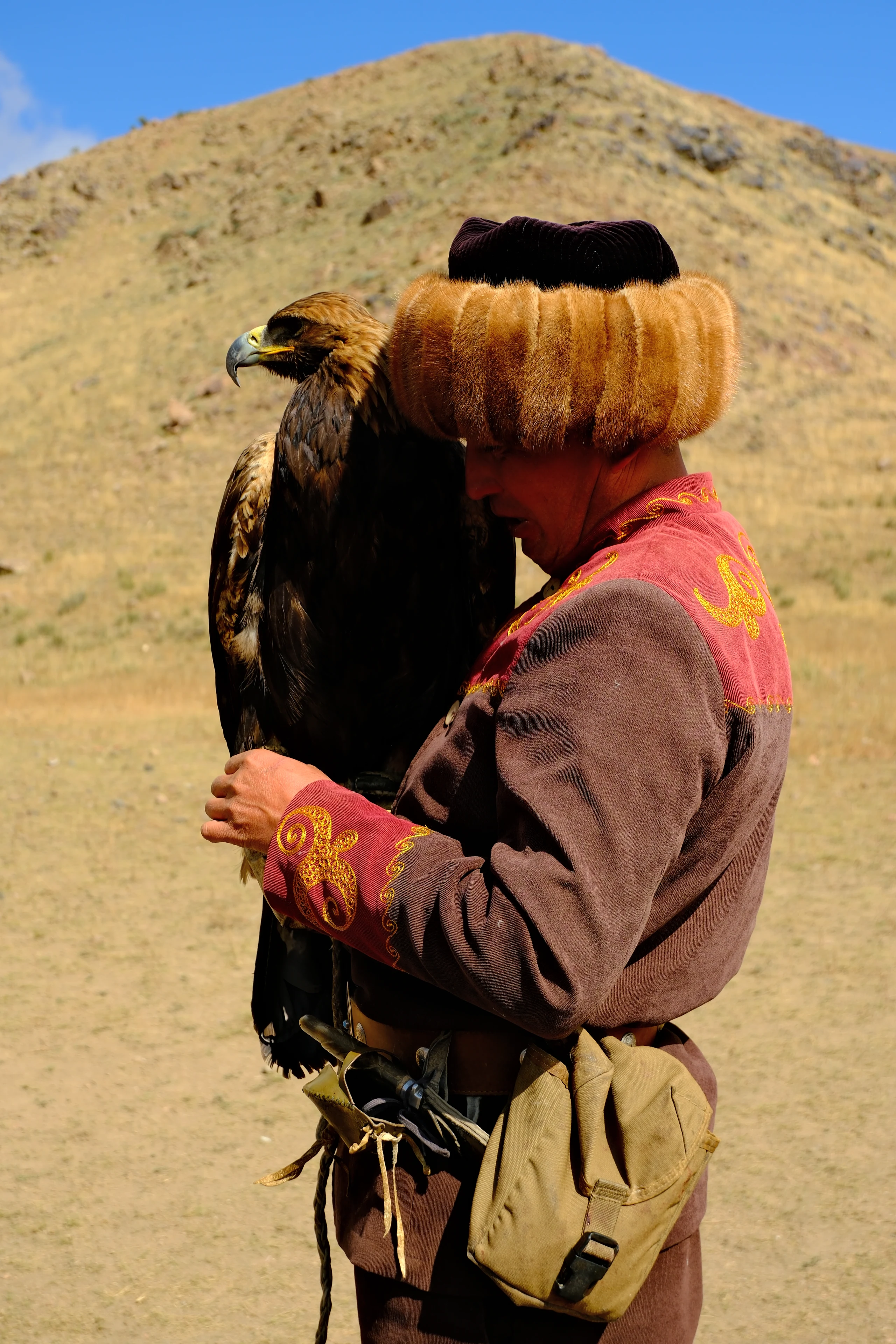 An eagle hunter holding a golden eagle against the mountain slopes.