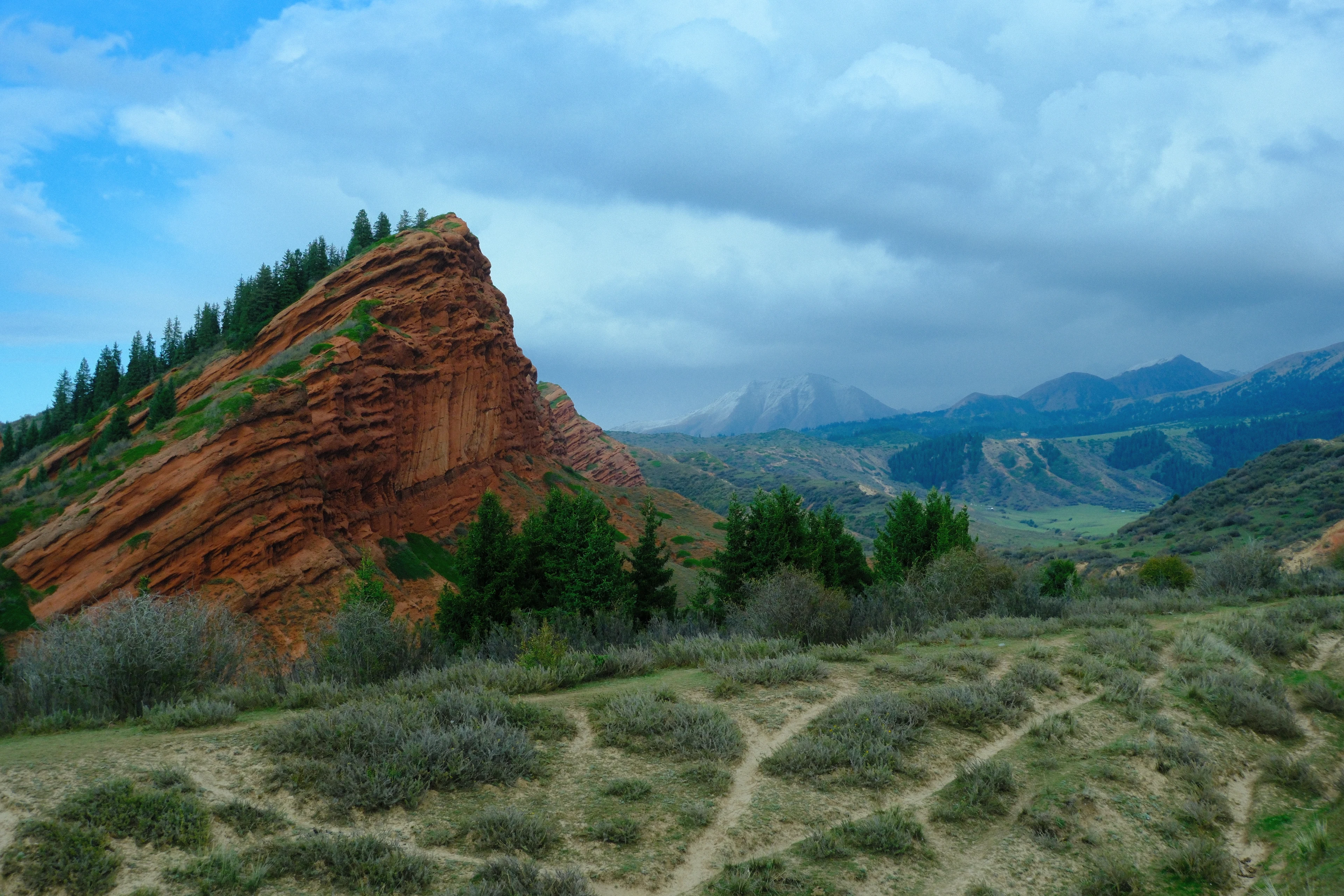 A red rock ridge, conifers and distant mountains at Jeti-Oguz.