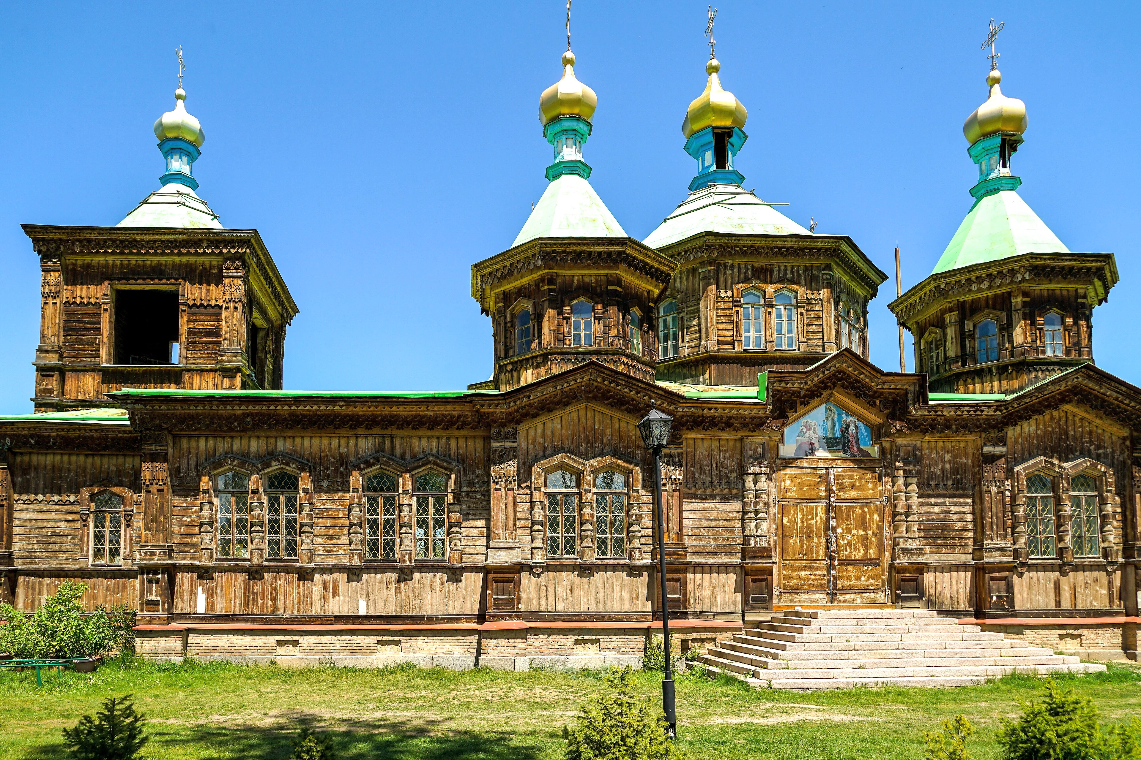 The wooden Holy Trinity Church in Karakol beneath a clear blue sky.