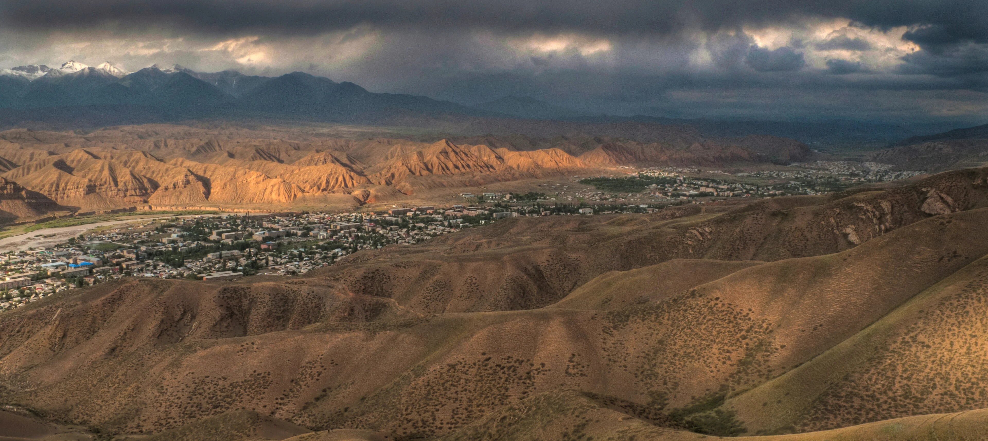 Naryn city seen from the southern hills beneath changing mountain light.